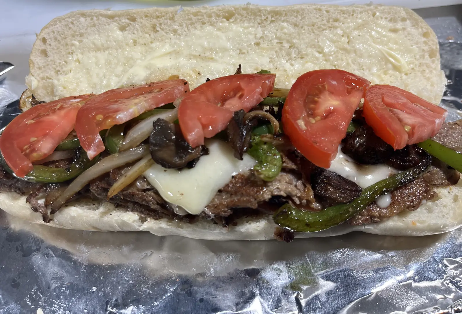 A loaded steak and cheese sub with peppers, onions, mushrooms, and tomato, made to order at Dinner Is Served