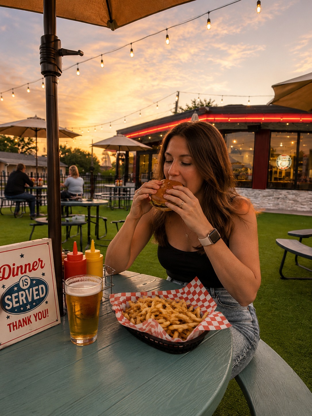 Guest biting into a cheeseburger with a side of fries on the patio at Dinner Is Served
